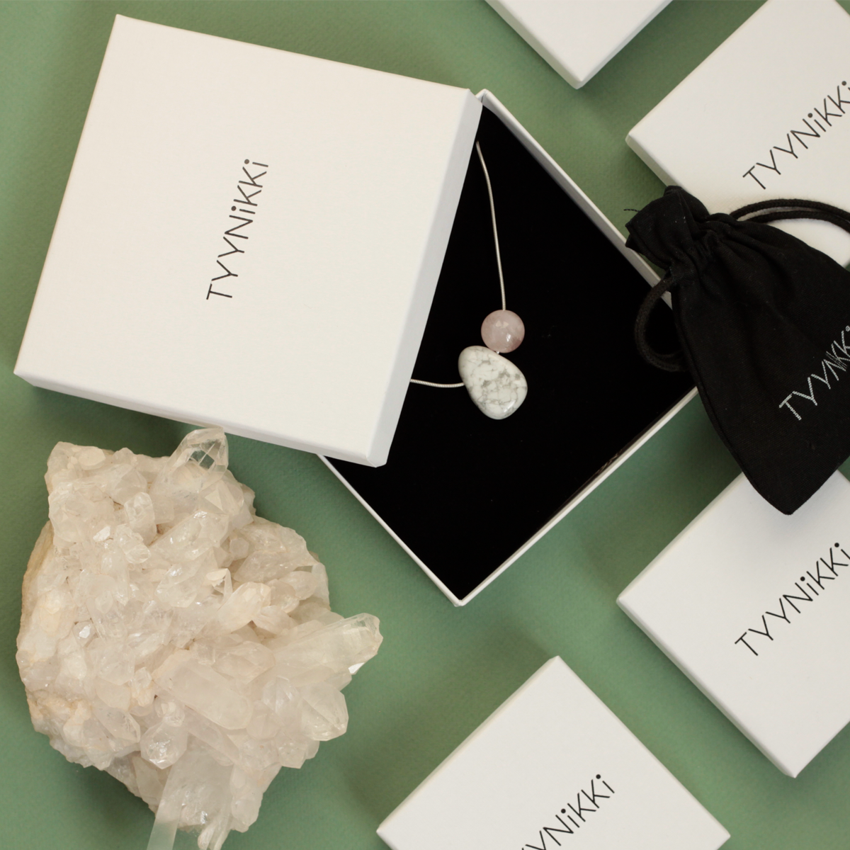 Tyynikki Jewellery Packaging Boxes, Pouch, Semiprecious Gemstone Jewellery Flatlay with a Clear Quartz Cluster and Green Backdrop