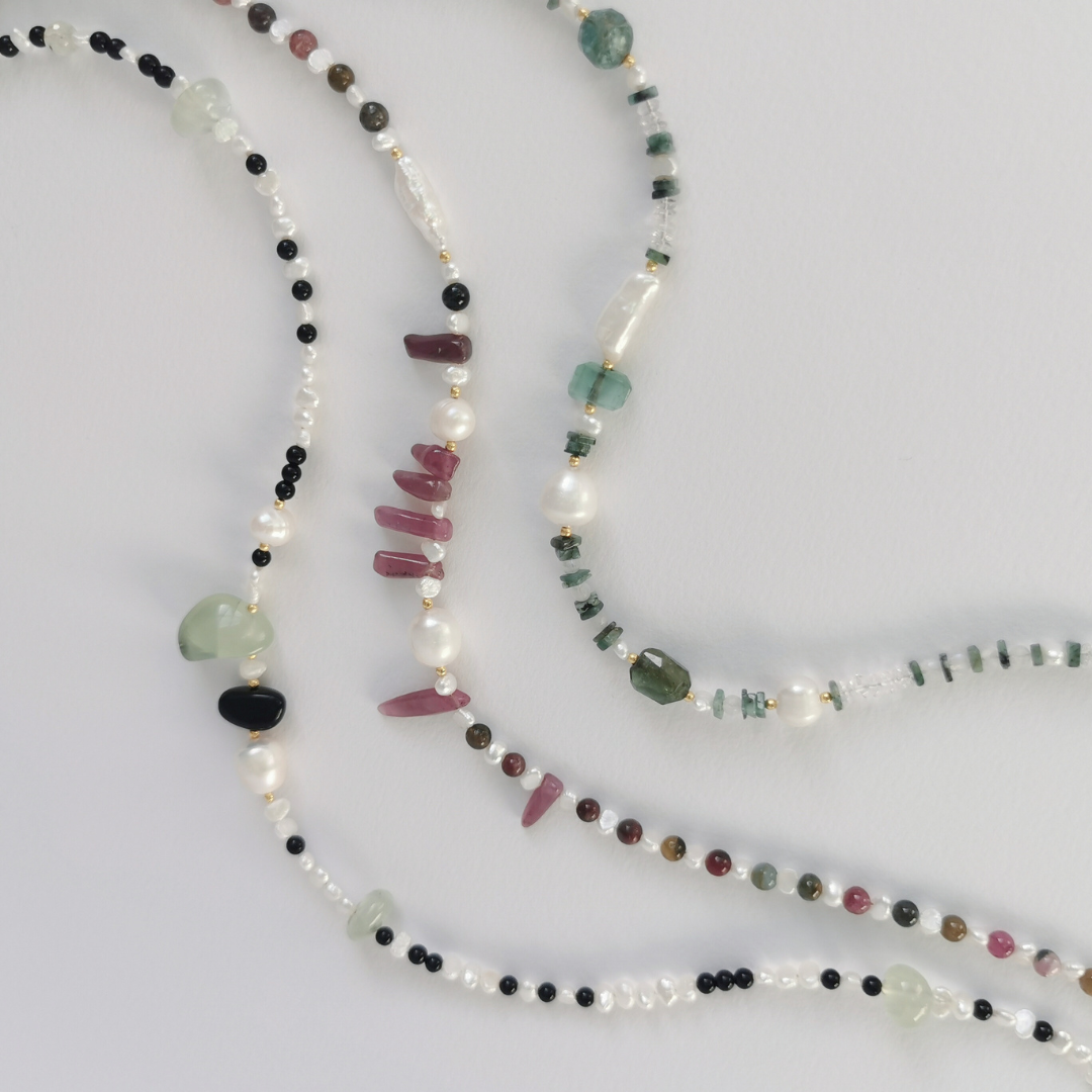 Three Layered Semiprecious Gemstone Bead Necklaces on a White Background, with Green Emerald, Green Tourmaline, Clear Quartz, White Rainbow Moonstone, White Freshwater Pearl, Pink Ruby, Multicoloured Tourmaline, Prehnite, Black Onyx and all Gold Vermeil Hardware